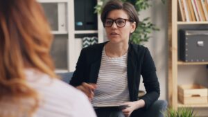 A thoughtful adult sits across from a therapist in a comfortable, well-lit office during a counseling session.