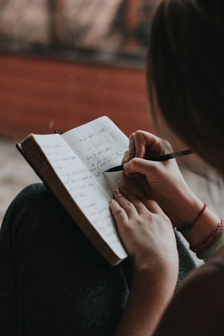 A person sitting by a window, writing in a journal with a mug of tea nearby, natural light filling the room.